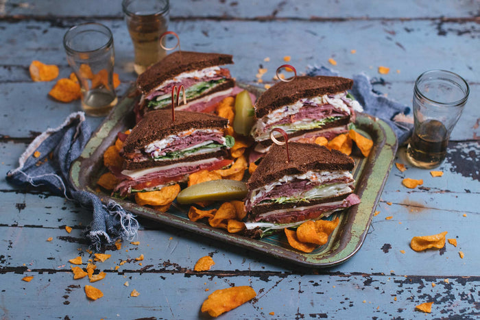 smoked meat club sandwich in pumpernickel brown bread surrounded by bbq chips